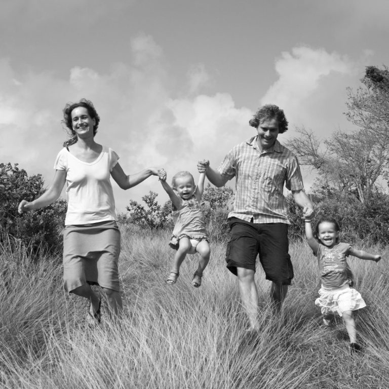 Eine Familie mit zwei Kindern hält sich an den Händen und läuft durch hohes Gras.