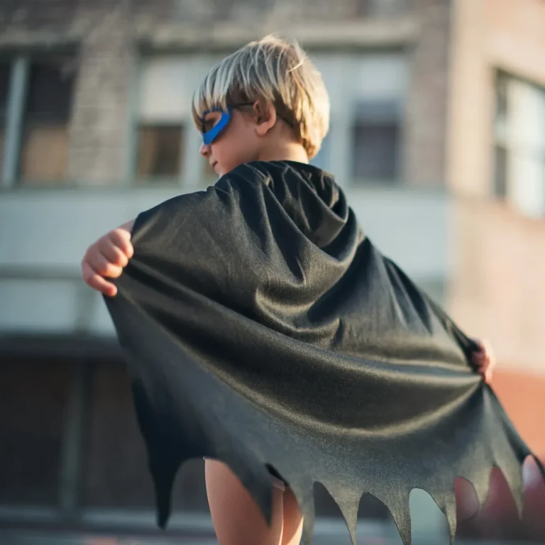 Warum Werte der Schlüssel zu resilienten Kindern sind Ein kleiner Junge in einem Superhelden-Kostüm mit Umhang und Sonnenbrille.