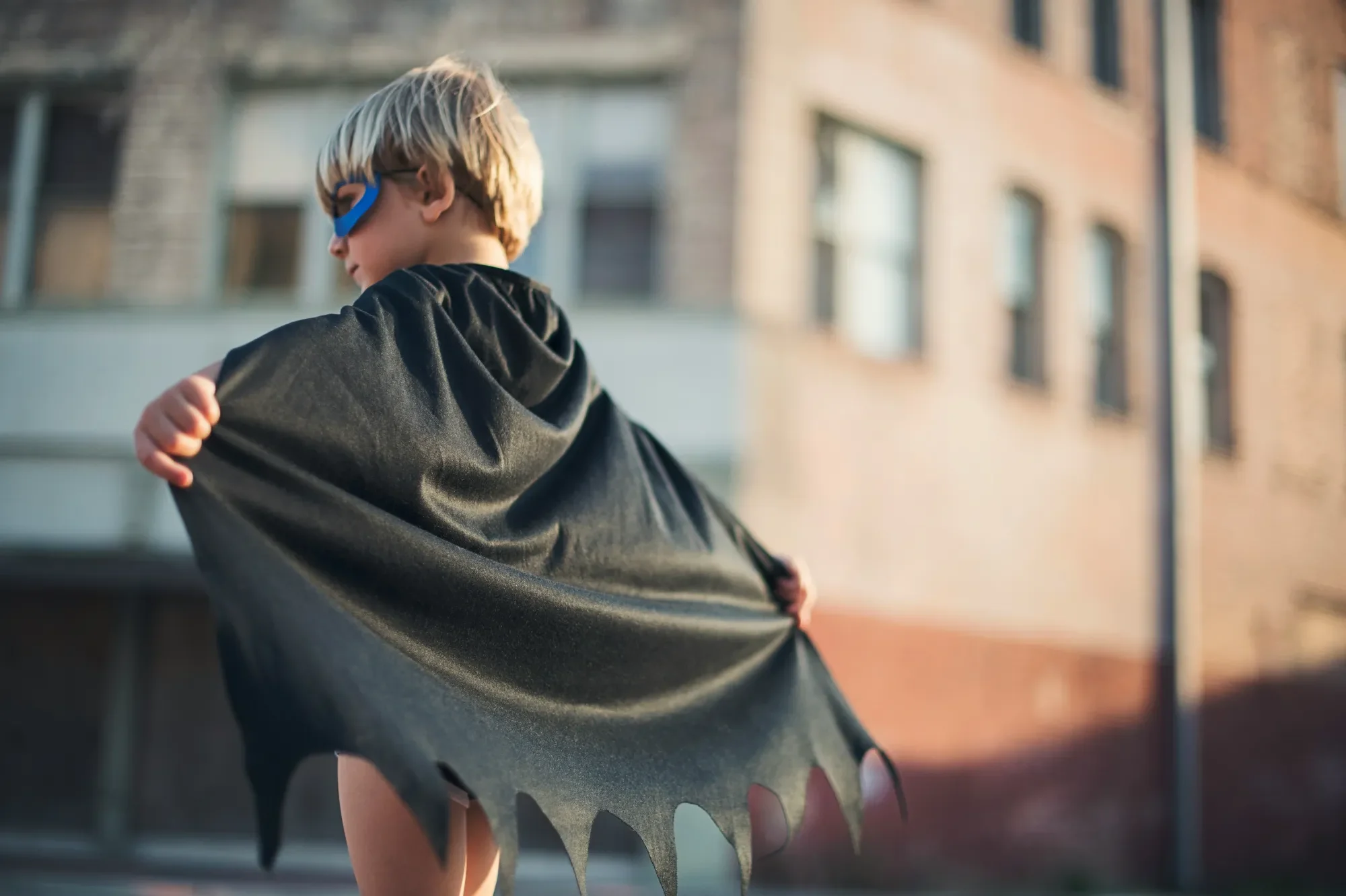Warum Werte der Schlüssel zu resilienten Kindern sind Junge mit Umhang und Sonnenbrille steht vor einem alten Gebäude und schaut zurück.