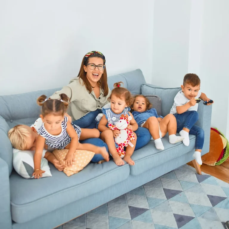 Spielerisch Werte vermitteln: So gelingt es im Alltag Eine Frau sitzt mit fünf Kindern auf einem hellblauen Sofa, alle lächeln und spielen.