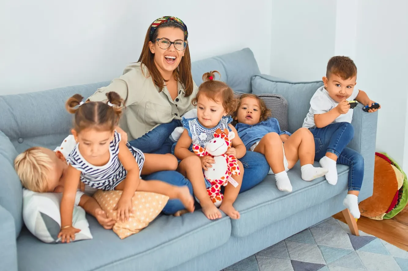 Spielerisch Werte vermitteln: So gelingt es mit Ihren Kindern Eine fröhliche Frau sitzt mit fünf Kindern auf einem grauen Sofa.