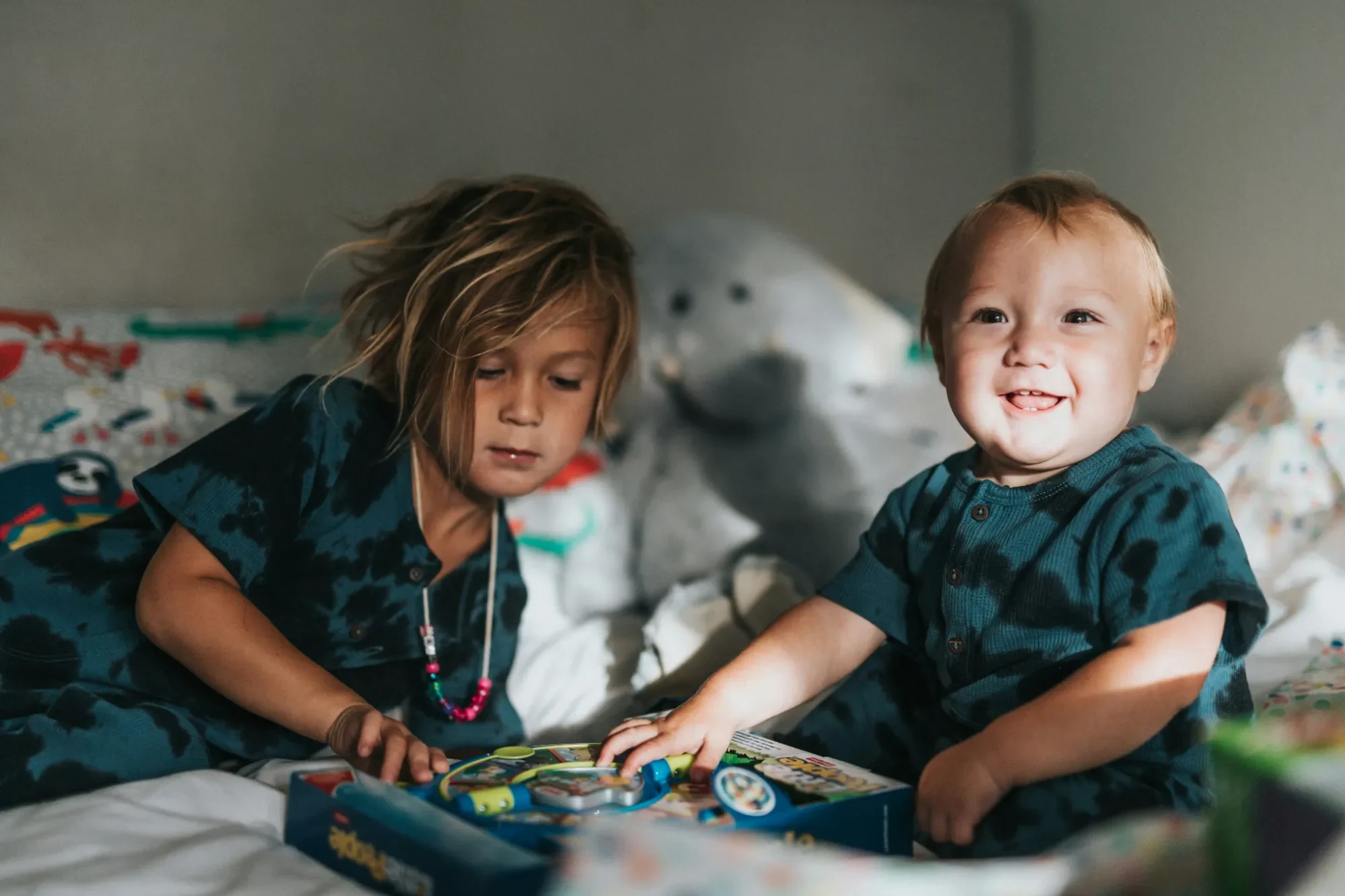 Warum Werte die Grundlage für eine glückliche Kindheit sind Zwei Kinder sitzen auf einem Bett und spielen mit bunten Spielzeug.