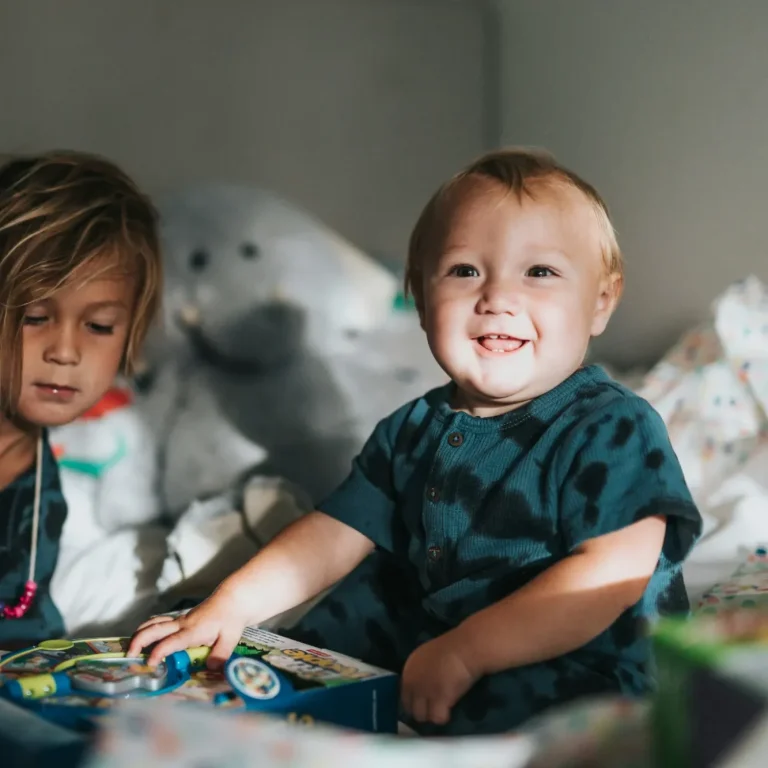 Warum Werte die Basis für eine glückliche Kindheit sind Zwei Kinder spielen im Zimmer, eines lächelt und hält Spielzeug in der Hand.