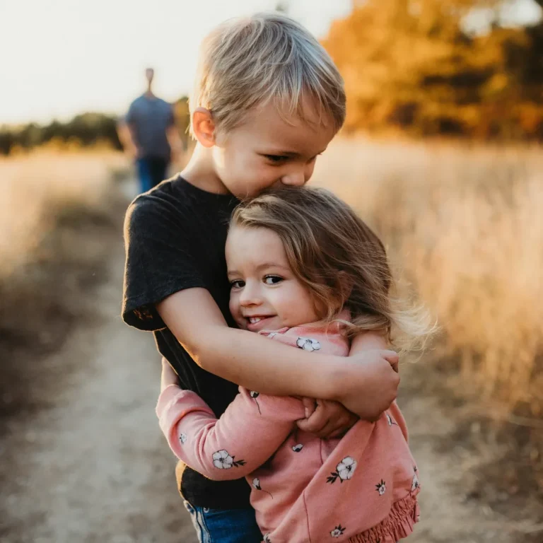 Five easy ways to teach kids kindness and respect at home Ein Junge umarmt ein Mädchen auf einem Feldweg in der Abenddämmerung.