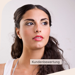 Kundenbewertung Lächelnde Frau mit blonden Haaren sitzt an einem Tisch neben einer Pflanze.
