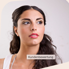 Lächelnde Frau mit blonden Haaren sitzt an einem Tisch neben einer Pflanze.