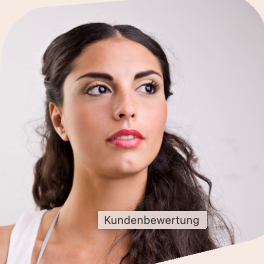 Lächelnde Frau mit blonden Haaren sitzt an einem Tisch neben einer Pflanze.